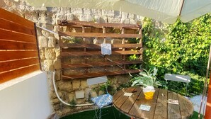 A cozy outdoor seating area with two wooden tables and chairs, surrounded by a stone wall and lush greenery. - 1 Bedroom Apartment in Pozzuoli (Pozzuoli)