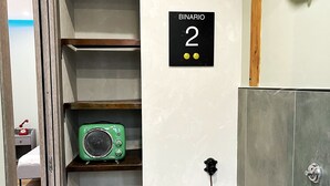 A compact bathroom with a toilet, a sink, a green radio, a shelf with toiletries, and a trash bin. - 1 Bedroom Apartment in Pozzuoli (Pozzuoli)