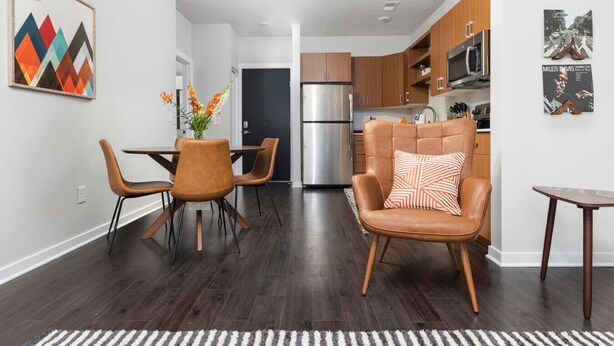 A modern kitchen with wooden cabinets, a stainless steel refrigerator, and a dining area with a table and chairs.