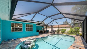 Piscina com área de estar coberta, parede externa azul e vista para casas vizinhas.