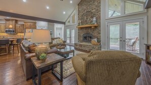A spacious living area with a stone fireplace, wooden flooring, and a ceiling fan.