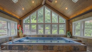 A hot tub in a room with large windows, wooden ceiling, and stone flooring.
