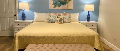 A bedroom with a large bed, two nightstands with lamps, a bench, and a wall painting.