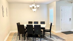 Uma área de refeições com uma mesa branca, cadeiras pretas, um candelabro e um tapete estampado.
