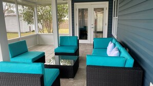 Eine überdachte Terrasse mit Türkis-Kissenstühlen und einem Glastisch, mit Blick auf den Garten.