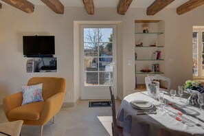 A dining area with a table set for four, a television mounted on the wall, and a bookshelf with decorative items.