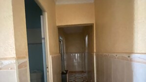 A narrow hallway with patterned floor tiles, a door leading to a bathroom, and a tiled wall.