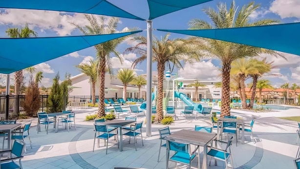 A resort pool area with blue umbrellas, palm trees, and lounge chairs. - New 12 BD W/heated pool home-12 min to Disney 2480 (Kissimmee)