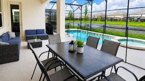 An outdoor patio with a pool, seating, and a view of a residential area. - New 12 BD W/heated pool home-12 min to Disney 2480 (Kissimmee)