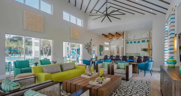 A spacious lobby with a bright, open design, featuring a yellow sofa, blue chairs, and a wooden coffee table. - New 12 BD W/heated pool home-12 min to Disney 2480 (Kissimmee)