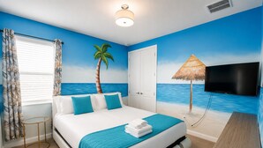A bedroom with a bed, a TV, a window with curtains, a door, and a wall mural of a beach scene. - New 12 BD W/heated pool home-12 min to Disney 2480 (Kissimmee)