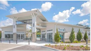 A modern building with a covered entrance, large windows, and a landscaped area with small trees. - New 12 BD W/heated pool home-12 min to Disney 2480 (Kissimmee)