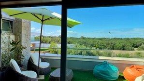 Varanda com cadeiras de vime, um guarda-sol verde e espreguiçadeiras.