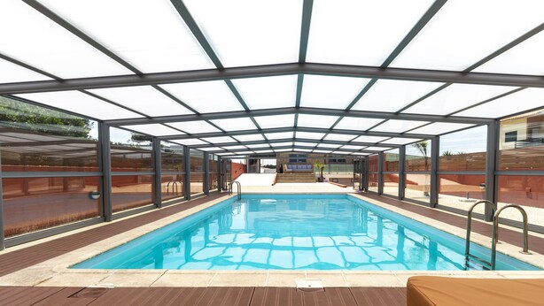 Piscina interna com teto de vidro e deck de madeira.