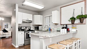 Uma cozinha moderna com armários brancos, bancada de granito e uma ilha central com banquetas.