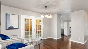 Uma sala de estar ampla, com um sofá branco, uma mesa de centro de vidro e um lustre.
