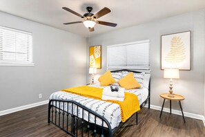 Ein Schlafzimmer mit einem Bett, einem Deckenventilator, einem Nachttisch und einem gerahmten Kunstwerk an der Wand.