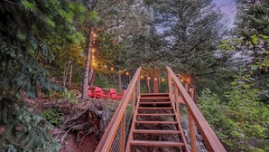 A wooden staircase leading up to a bridge in a forested area with string lights. -     Private Luxury Retreat in Evergreen, Hot Tub + Multiple Decks (Evergreen)