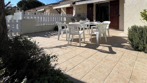 Eine Terrasse mit Tisch und Stühlen, ein weißer Zaun und ein Gebäude mit einem Ziegeldach.