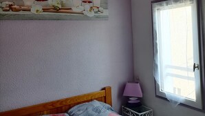 Ein Schlafzimmer mit Bett, Nachttisch, einem Fenster mit Vorhängen und einer Wandregal mit Dekoration.