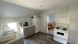 Kompakti keittiö, jossa on mikroaaltouuni, jääkaappi, liesi sekä ruokailutila pöydän ja tuolien kera.