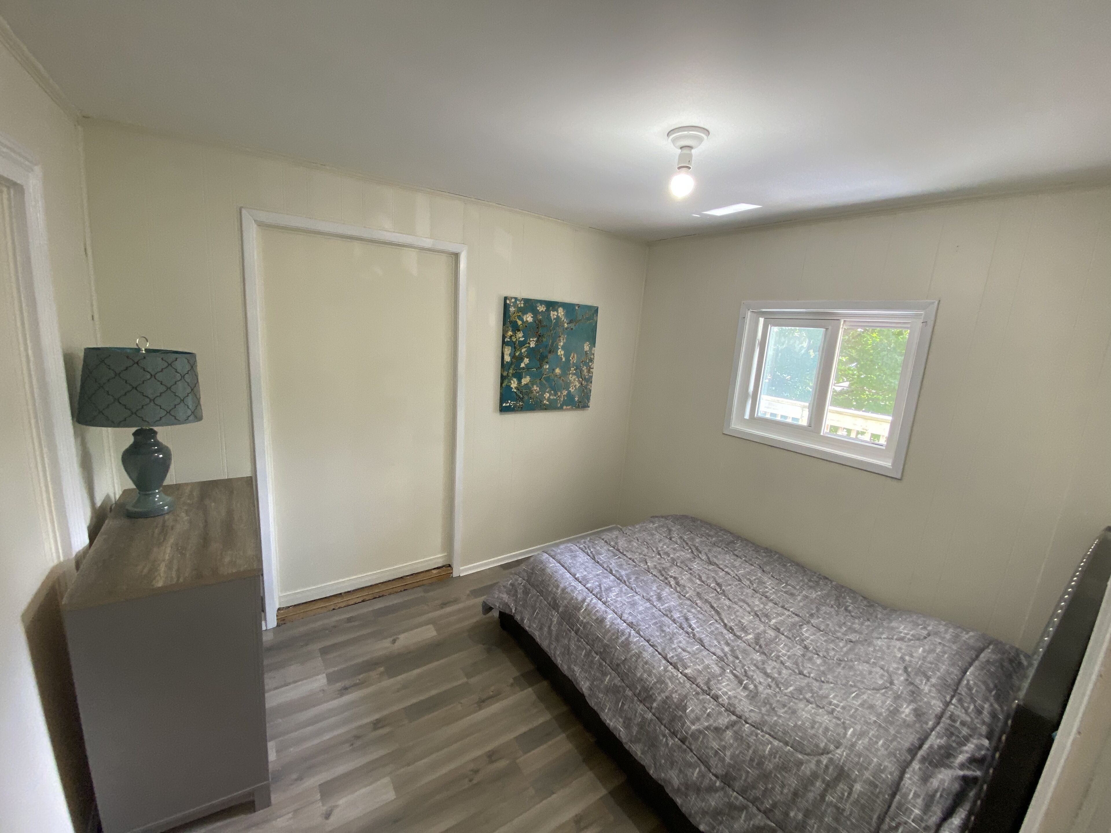 A bedroom with a bed, a nightstand, a window, and a ceiling light.