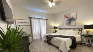 Quarto moderno com cama, mesas de cabeceira, televisão e um quadro na parede.