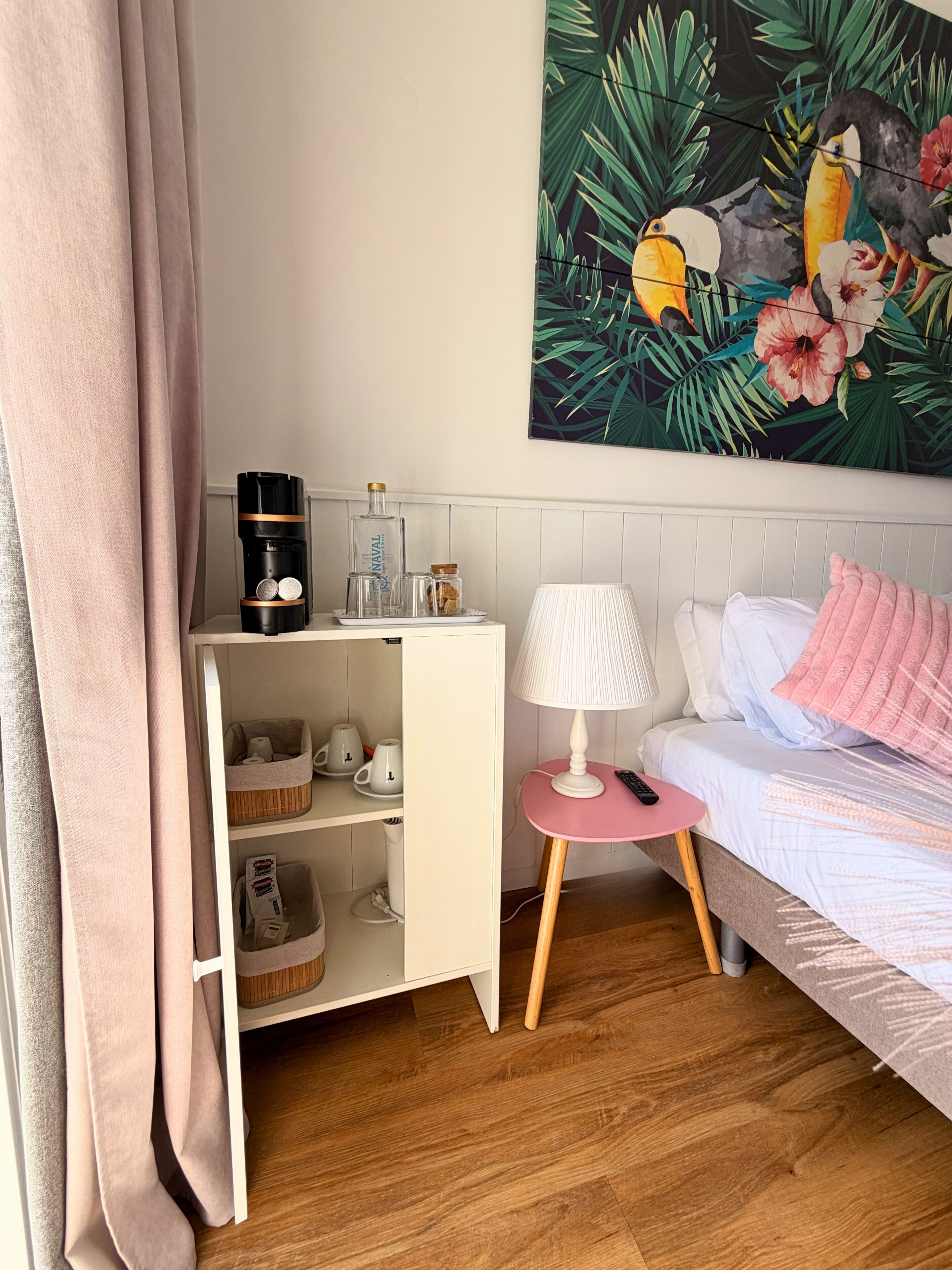 Ein ordentlich eingerichtetes Schlafzimmer mit Bett, Nachttisch, Lampe und einer Kaffeemaschine auf einem Regal.