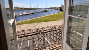Vista a través de un ventanal de un puerto deportivo con barcos amarrados, un área con césped y una barandilla metálica.