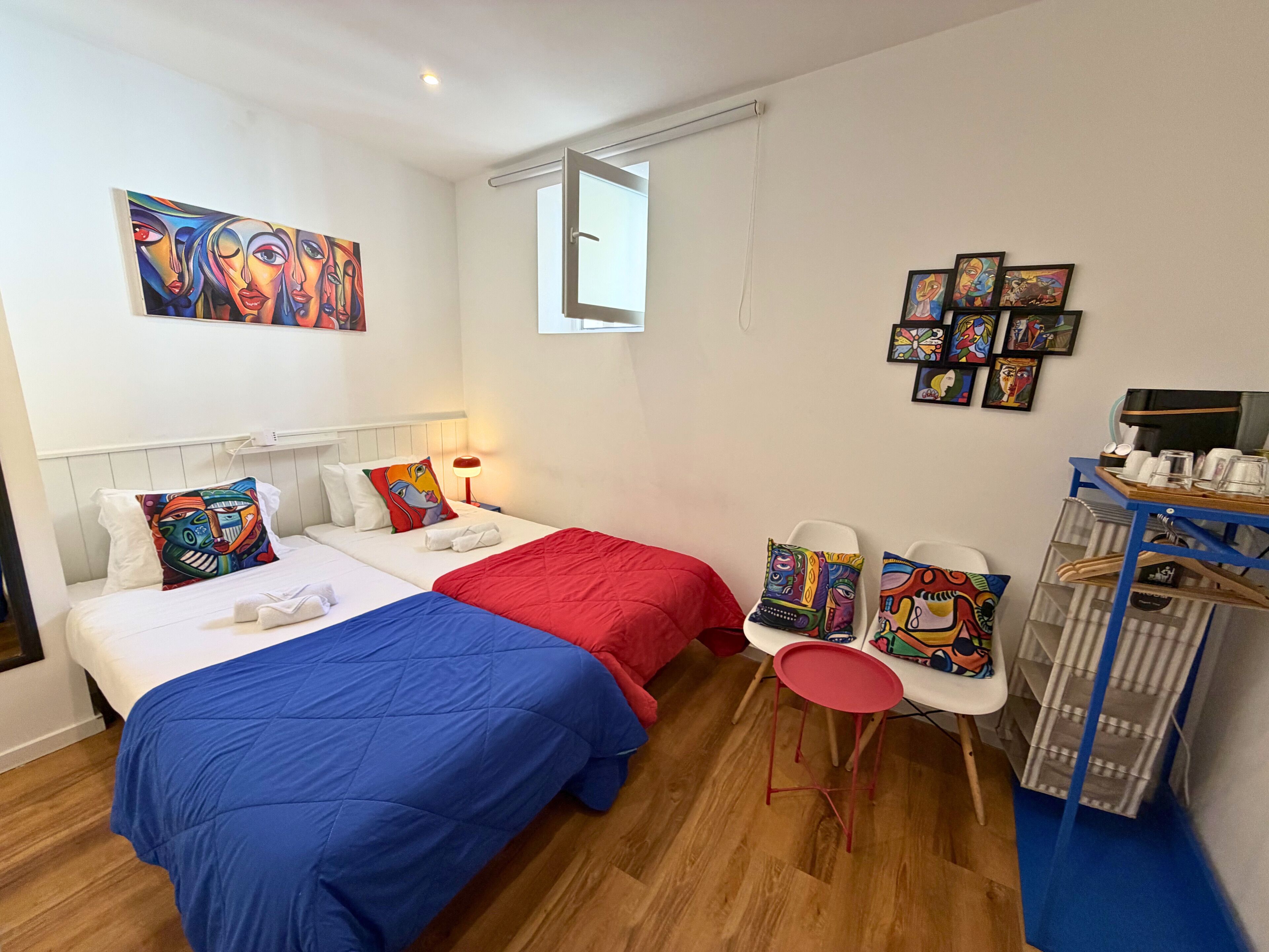 A hotel room with two beds, a small table with chairs, and artwork on the walls.