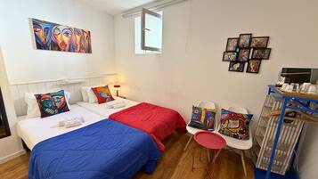 A hotel room with two beds, a small table with chairs, and artwork on the walls.