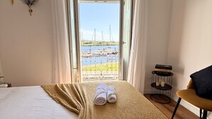 Habitación de hotel con cama, vista al mar, televisión y una mesita con candelabro.
