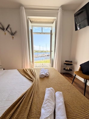 Quarto de hotel com uma cama, vista para o mar, televisão e uma mesinha com castiçal.