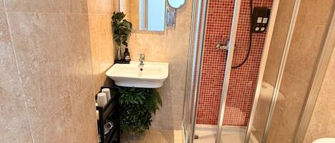 Un baño con cabina de ducha de vidrio, lavabo con espejo e inodoro.