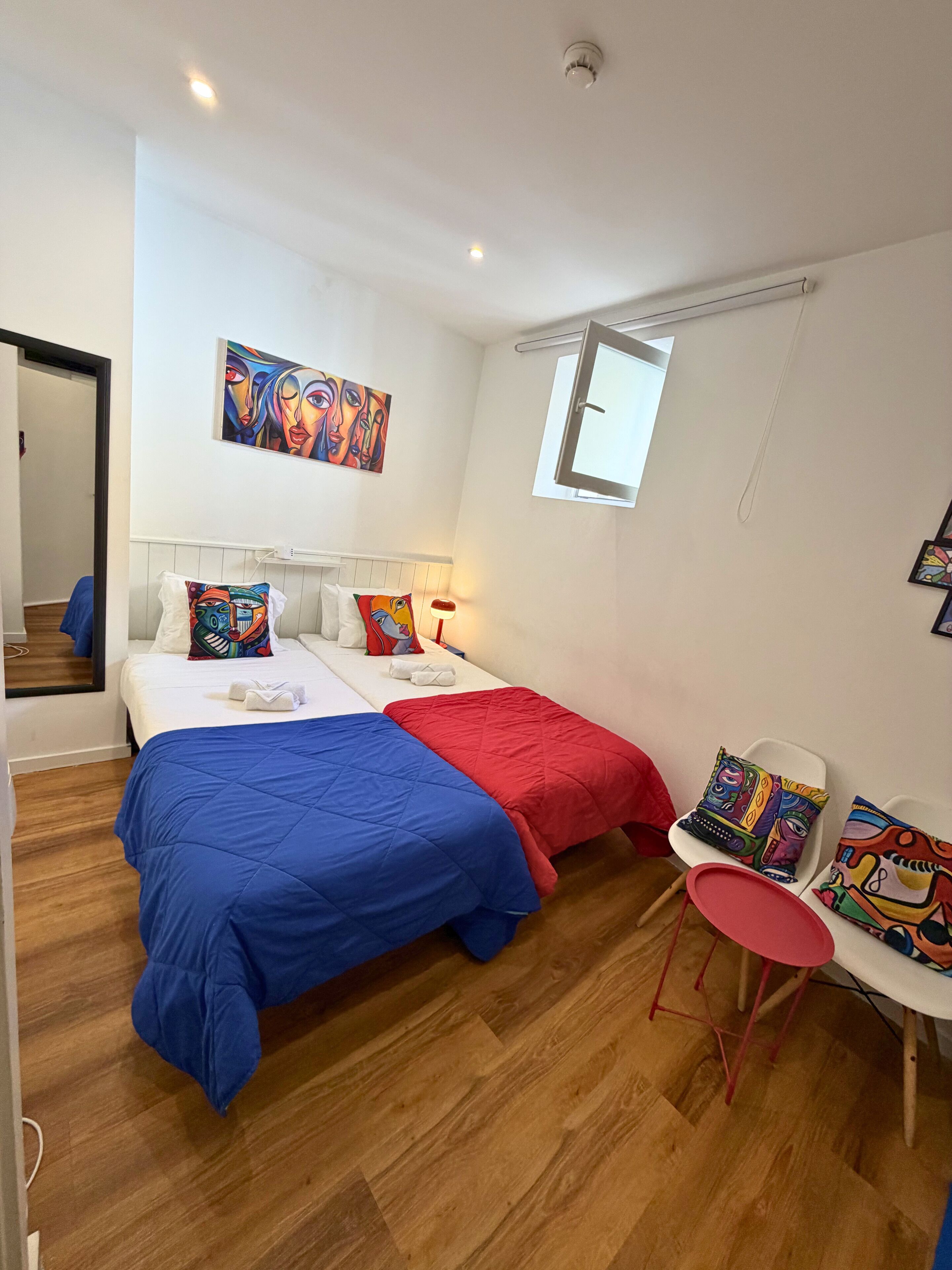 A room with two beds, a window, a chair, and a painting on the wall.