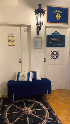 A hallway with a blue sofa, a ship's wheel decoration, a welcome sign, and a map on the wall. - Naval Guest House & Bistrô (Vila do Conde)