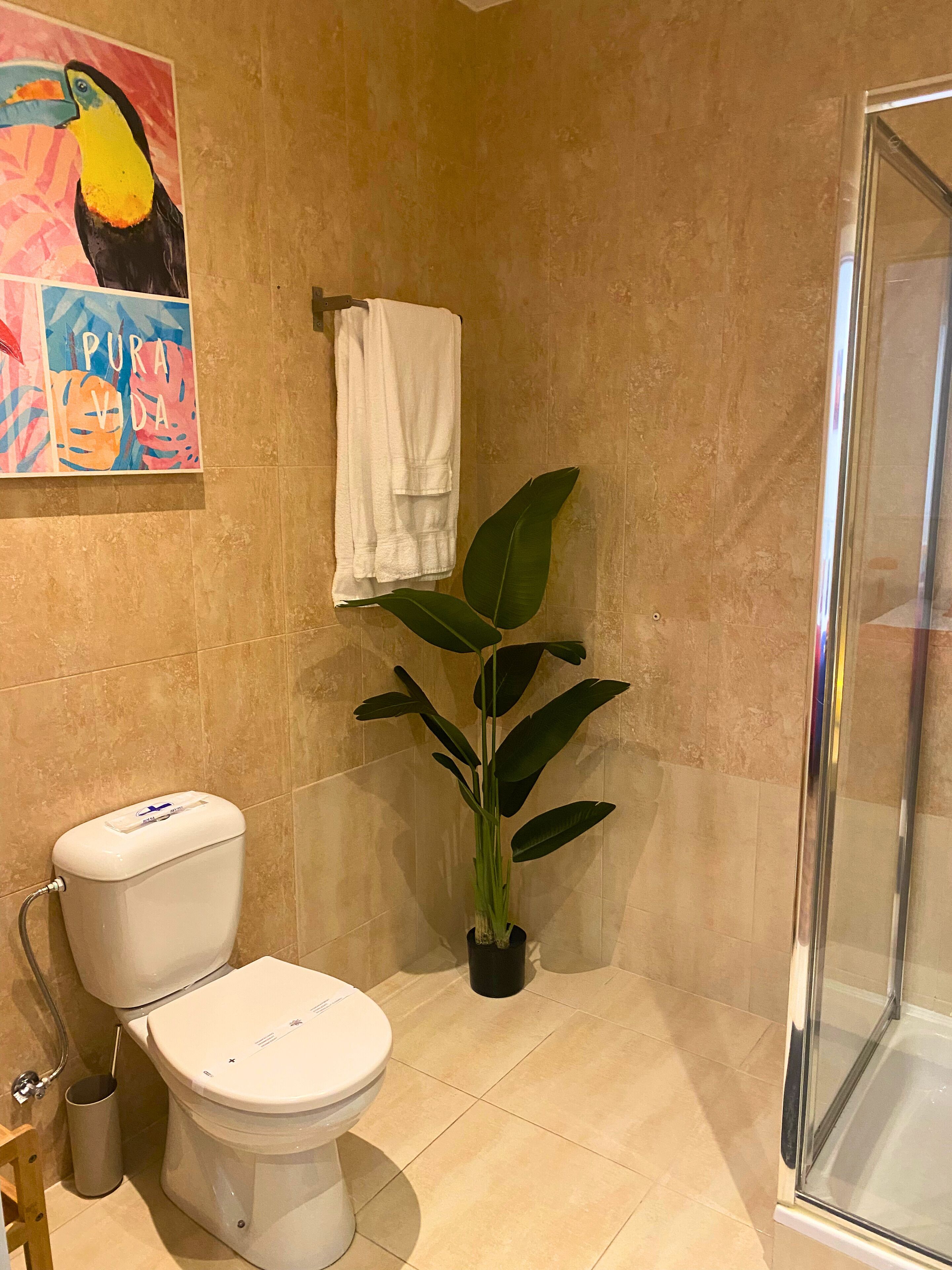 Un baño con inodoro, ducha, planta en maceta y una obra de arte colorida en la pared.