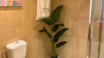 Un baño con inodoro, ducha, planta en maceta y una obra de arte colorida en la pared.