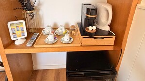 Una kitchenette compacta equipada con cafetera, tetera y un refrigerador pequeño.