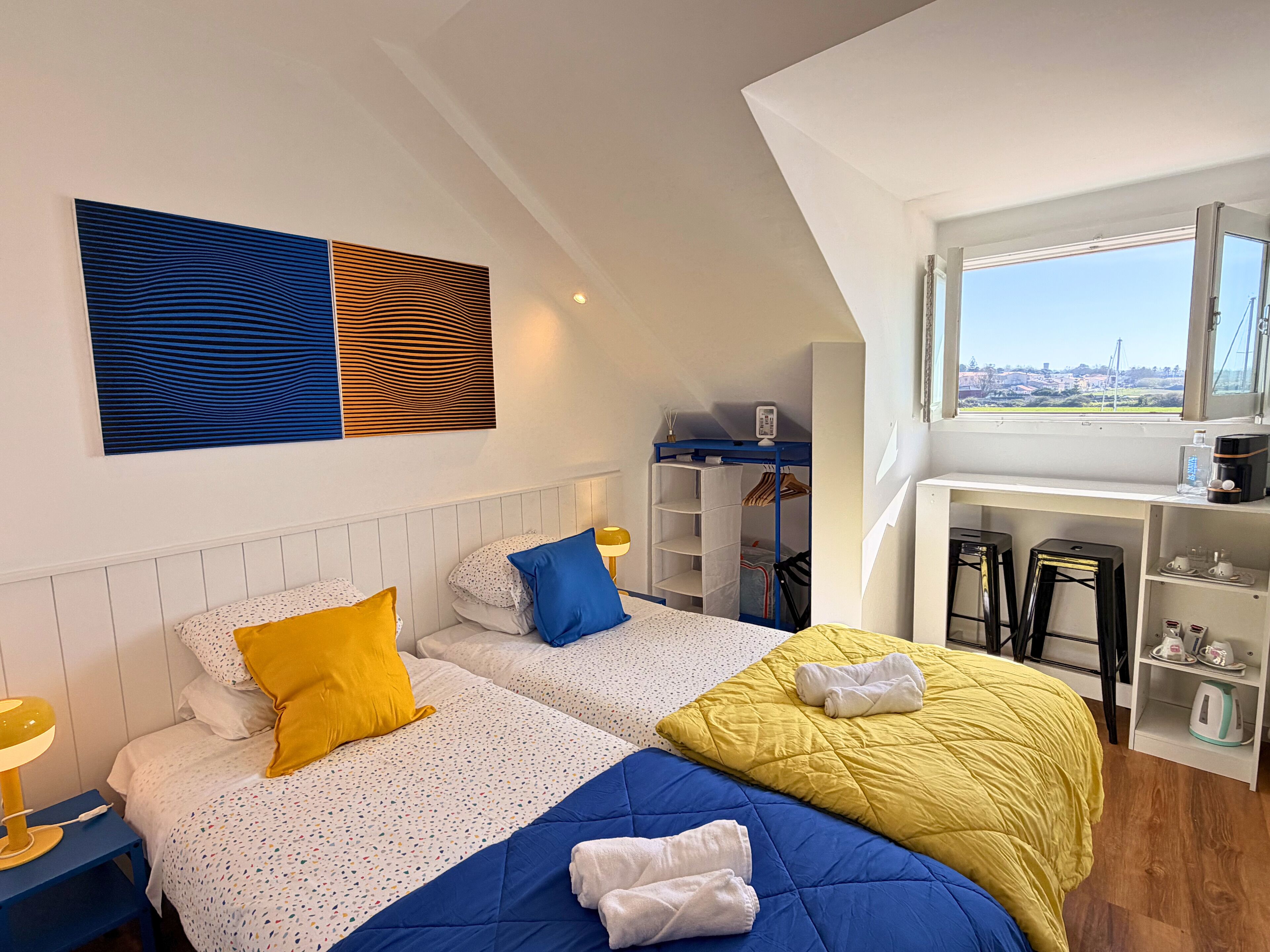 A modern bedroom with two beds, a desk, and a view of the city.