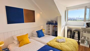 A modern bedroom with two beds, a desk, and a view of the city.