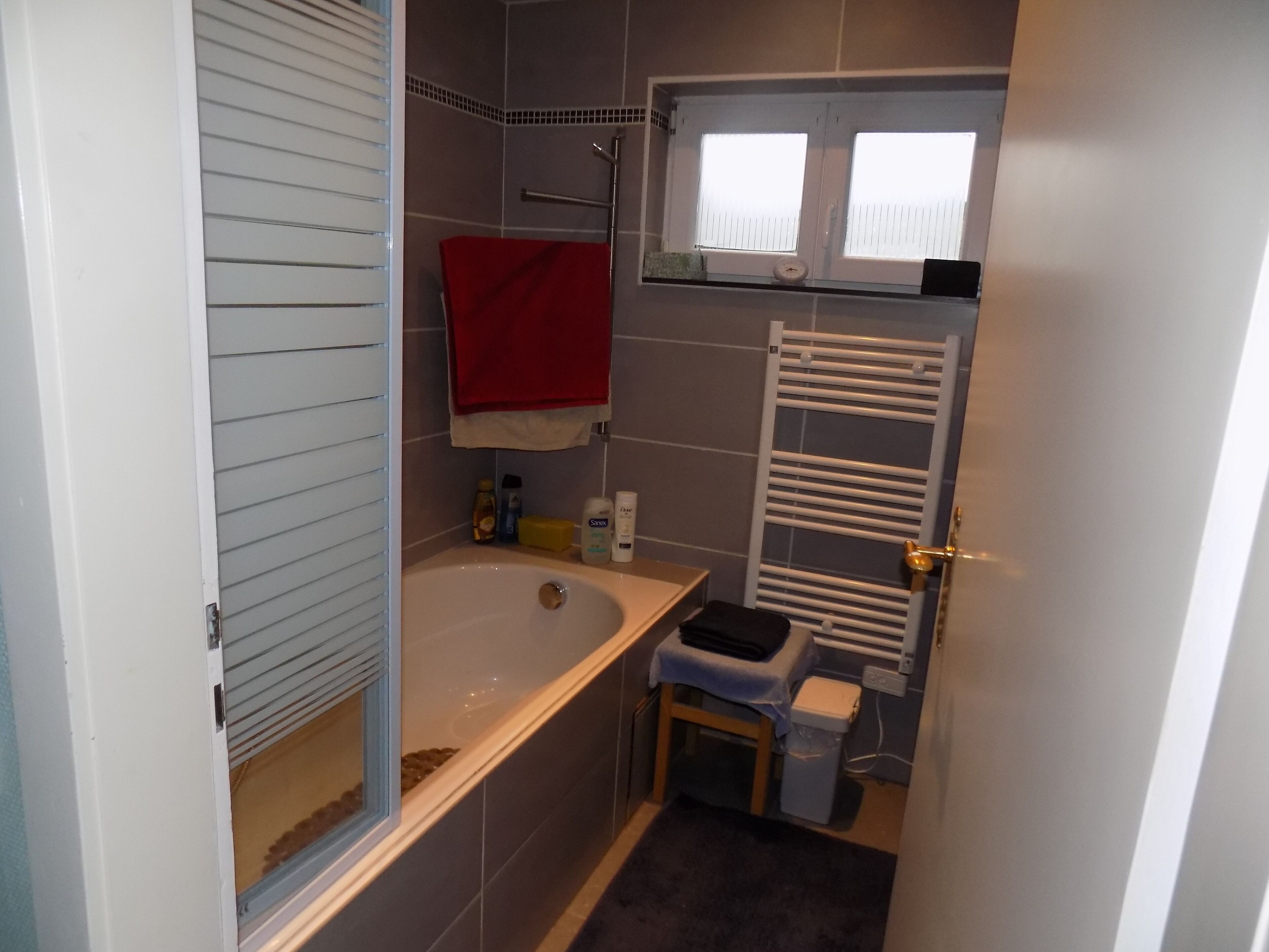 A compact bathroom with a bathtub, a small sink, a toilet, and a window above the toilet.
