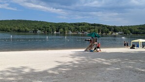 A lakeside beach with a wooden structure, a tent, and a boat in the background.