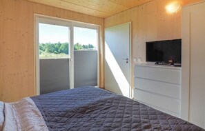 Relax in a serene bedroom with a large bed, TV, and sliding glass door leading to an outdoor area with a view of lush greenery.
