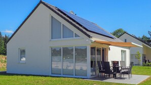 Une maison moderne dotée d’une grande porte vitrée, d’un patio avec des meubles d’extérieur et de panneaux solaires sur le toit.
