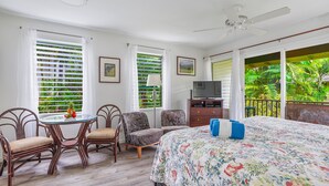 Une chambre à coucher comprenant un lit, un téléviseur, un bureau avec des chaises et de grandes fenêtres équipées de stores.