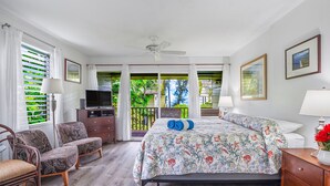 Une chambre avec un lit, une télévision, une chaise, un bureau et un balcon donnant sur un espace verdoyant.
