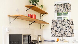 A kitchen with white cabinets, a microwave, a kettle, and a shelf with red cups and a plant. - La Maison 29 (Roseau)