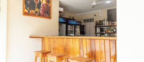 A bar area with wooden stools, a ceiling fan, and a painting on the wall.