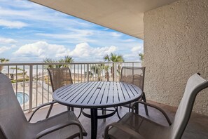 A round table with metal chairs on a balcony with a view of palm trees and a distant building. - White Sands and Good Times (Orange Beach)